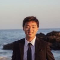 Student Steven Vu in a black suit and tie with water view in background