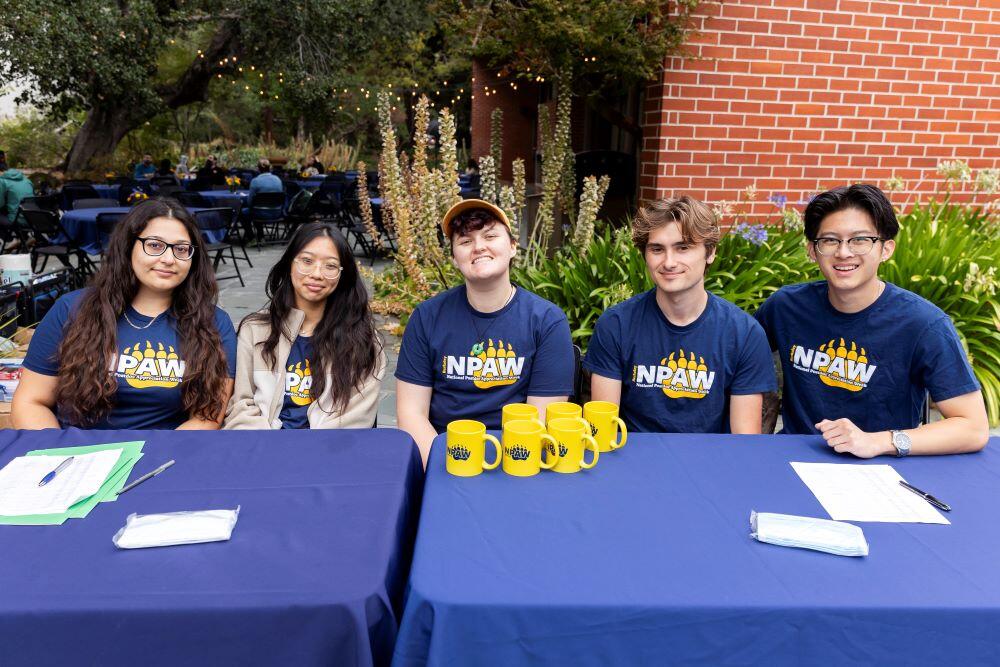 Five VSPA students at the registration table with blue cover and yellow mugs on top.