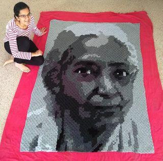 Kanika Khanna sitting next to textile quilt of a person's face.
