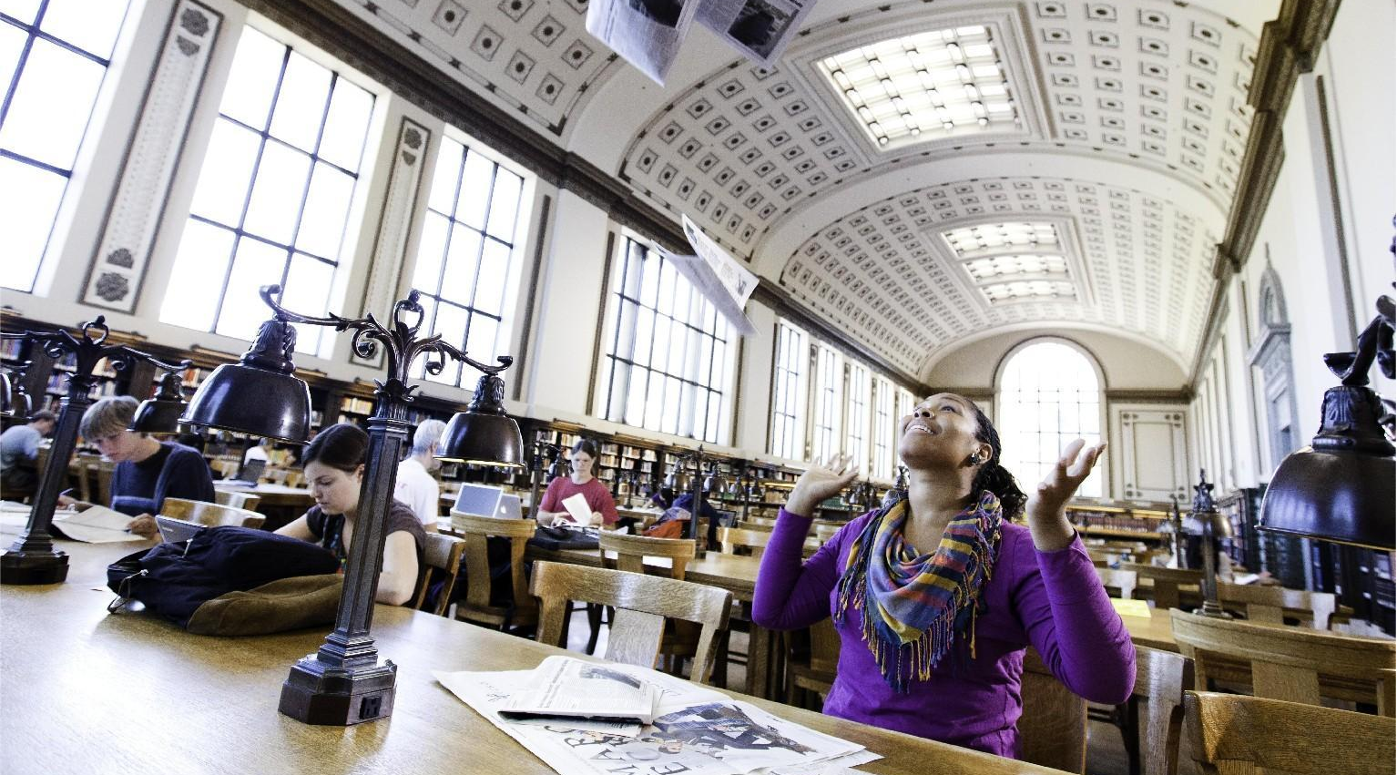 Student happily tossing papers in air inside of UC Berkeley library