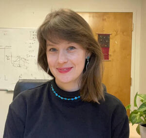 Dr. Carol Little Rose sitting on an office chair with a door and whiteboard in the background