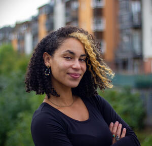 Dr. Laura Lewis headshot wearing a blue shirt and crossing arms with blurred buildings in background