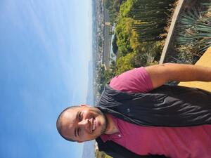 Joaqin Urrego wearing a red shirt and black vest jacket with a city vista in the background.