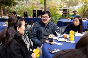 Postdocs sitting around a table enjoying coffee and pastries in outdoor patio.