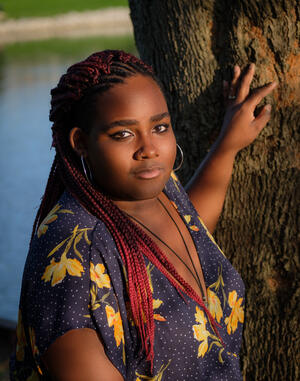 Dr. LaVelle Ridley standing in front of and touching a tree with a water source in the background.