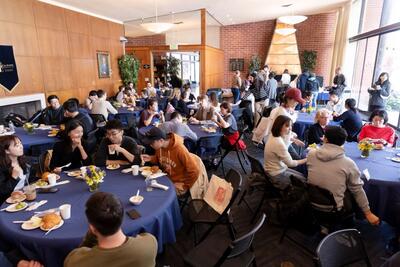 Wide shot of scholars sitting around tables and chatting with each other at the welcome event