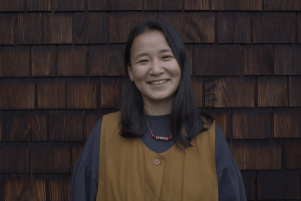 Choekyi Lhamo standing in front of brown shingled building in a tan and blue top.