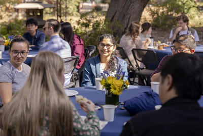 Postdocs sitting around a table enjoying coffee and pastries in outdoor patio.