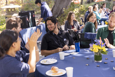 Postdocs sitting around a table enjoying coffee and pastries in outdoor patio.