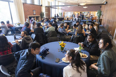 Wide shot of postdocs sitting around tables and chatting with each other at the PostdocFest event.