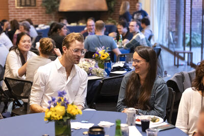 Two postdocs chatting at table with other PostdocFest attendees in the background.